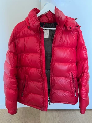 Moncler Maya Röd  - Säljer min jacka eftersom vintern är slut, den hade behövt lämnas på kemtvätt för att få ett 10/10 skick men allt är helt och det är inga skador på jackan  Storlek är 3 vilket motsvarar M/liten L Lämna ett prisförslag 😊 Har kvitto från NK Göteborg