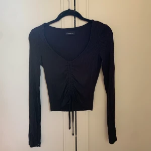 Topp - Svart långärmad topp med dragsko på mitten. Ribbad. Använd 1 gång.