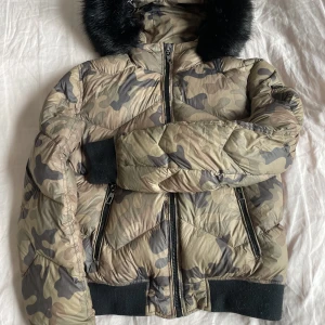Vinterjacka tjej stl ca 150 cm (Medium), kamouflage  - Jättesnygg kort vinterjacka, kamouflagefärgad från River Woods. Storlek M, passar 11-12 år, ca 150 cm  Huva med fuskpälskrage. 