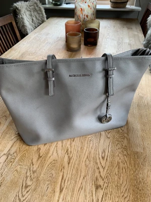 Väska | Michael Kors - Grå väska från Michael Kors. Bra storlek för dator/jobb. Smarta fack i väskan. Utmärkt skick ut och invändigt, dock lite slitet på handtagen som sista bilden visar. 