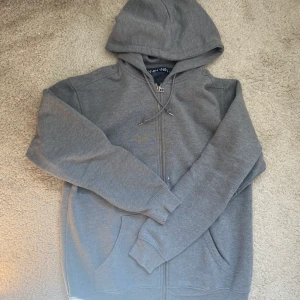 Grå Zip Hoodie - Säljer en grå zip hoodie i bra skick med inga defekter köpta från carlings, skriv om du har en fundering