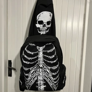 skelett ryggsäck - super cool ryggsäck med skelett 🦴på sidorna finns varsin ficka med ett skelett av en hand på, framsidan är revben och bröstkorg, och sedan finns det en luva med en dödskalle på. luvan går att ta av och på! på insidan finns flera fickor till! från bluefox 