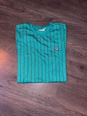 Randig T-shirt  - Helt ny och oanvänd T-shirt från FILA i mörk grön-blå.   Rensar ur min garderob från en hel del oanvända kläder🌼 Kika och se om du ser något mer i min profil som du gillar så skickar jag med det till dig också!😊 Fler kläder kommer! 