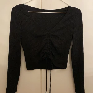 Svart kortare tröja - En super fin svart tröja som är  V-ringad, lite kortare och har en knytning på framsidan. Har aldrig använt den och är lite osäker på storlek men skulle säga S eftersom den sitter bra på mig som har S i storlek❤️