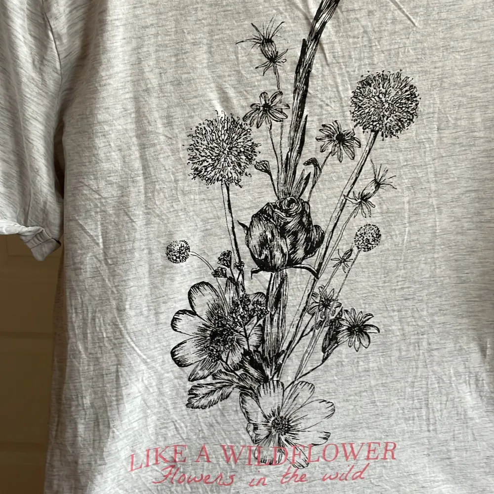 Tunn och somrig med blommor på ryggen. Lite text på framsidan. Armarna är upprullade precis i kanten. Köpt på H&M🐰🦋🩷. T-shirts.