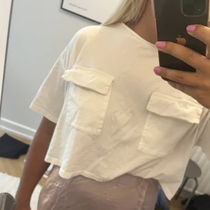 Vit T-shirt  - Vit t-shirt med fickor framtill. Snyggt croppad. Har inte kommit till användning 