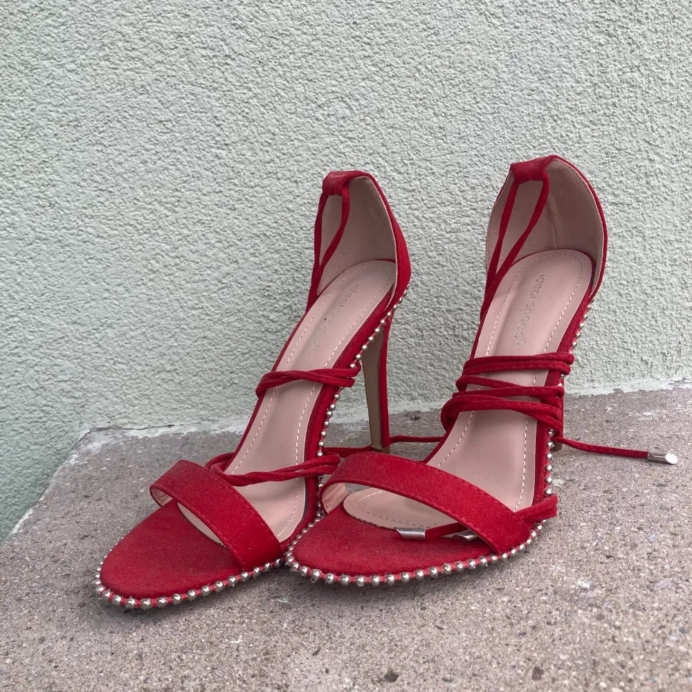 Röda stilettklackar med ”pärlor” längs sidorna och knytningar upp på benen. Aldrig använda, endast provade. Skor.