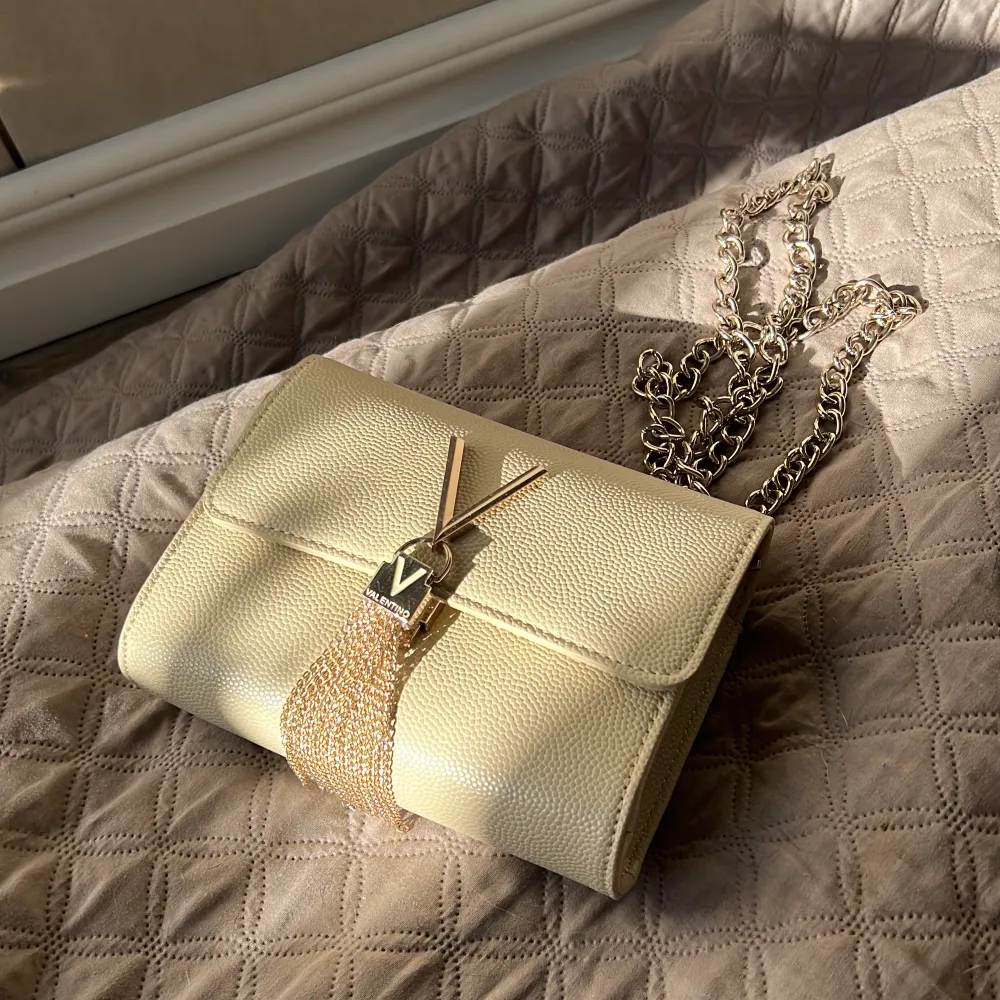 Snygg och enkel Valentino väska med snygga detaljer. Får fint plats med telefon, plånbok osv. Ny pris 1069kr, ser mer gul ut på bilden men är off white🫶🏻 använd 1 gång i bröllup och till en student bara🥰. Väskor.