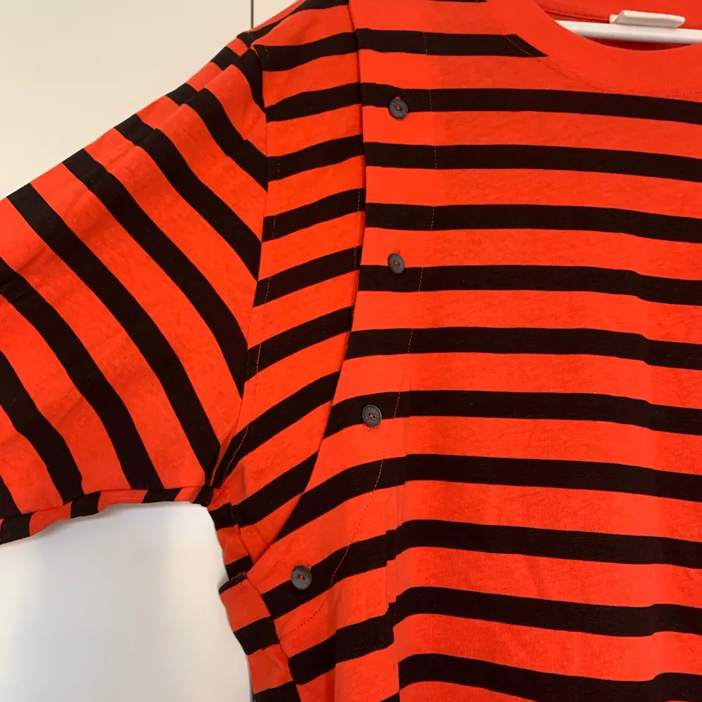 Never been used orange and black striped H&M studios T-Shirt in a thicker cotton quality. Oversized and removable sleeves with buttons on each arm. . Tröjor & Koftor.