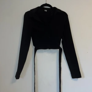 Svart blus med V krage  - En svart blus med snöre man kan knyta runt magen två varv. Något nopprig 