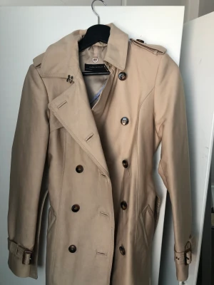 Trenchcoat Zara - Trenchcoat ifrån Zara, i en medellång längd. I använt skick, köpt för 999. I storlek XS