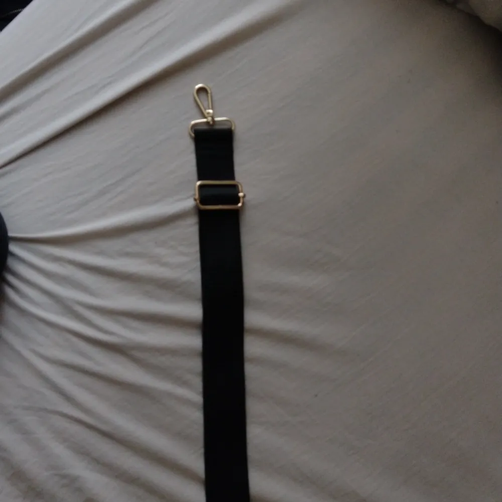 En svart axelrem till väska, aldrig använd, den är svart med guldiga knippen på, den är sjusterbar och kan göras längre. . Väskor.