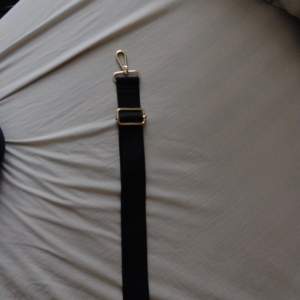 En svart axelrem till väska, aldrig använd, den är svart med guldiga knippen på, den är sjusterbar och kan göras längre. 