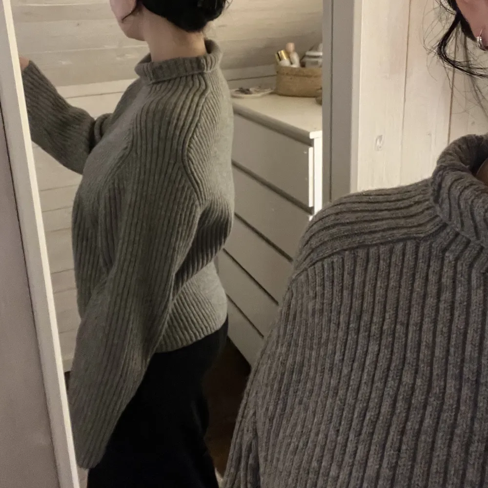 En grå ribbstickad tröja som är i lite kortare modell. Den har en hög krage (jag har vikt ner den) och vida ärmar. Perfekt nu till hösten! . Stickat.