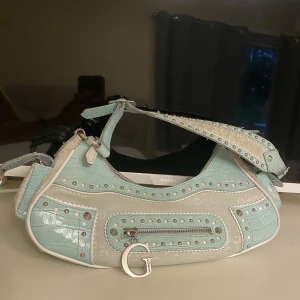 Guess väska - Häftig Guess väska som fått många komplimanger. Saknar en nit på varsin sida av de två fickorna på sidan men går enkelt att köpa o fixa. Fler bilder finns privat 🩷direktköp: 400kr 