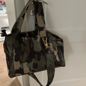  Hundväska camouflage från Gustaf & Evita - Hundväska camouflage från Gustaf & Evita i nyskick säljes.   Mått: ca L 36 x B 22 x H 24-29 cm  Passar liten hund. 