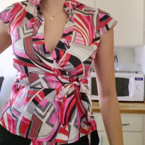 Färgglad knytblus - Inköpt mellan 2000-2012. Fantastiskt fin skjorta i röd och rosa design som knyts i midjan. Glansig sidenkänsla på tyget. Nyskick. Svarar på alla frågor.