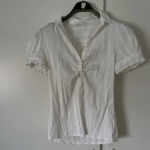 Kortärmad skjorta  - Superfin kortärmad skjorta/topp, med en fin detalj över bysten och räder med tunna guld kanter. Passar både till vardags eller finare tillfällen.