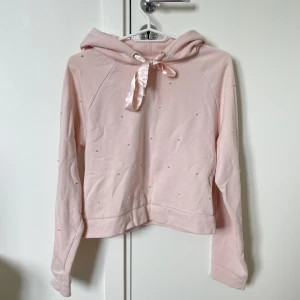 Hoodie - Rosa hoodie med pärlor på, även rosett vid halsen. Dock är jag osäker på storleken, men kan vara Xs/S.