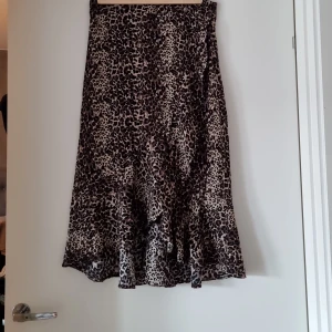 Snygg kjol med volang fram. - Kjolen är lite längre bak och har volang framtill. Dragkedja på sidan.