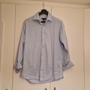 Slimfit skjorta - En slim fit skjorta i strl M från dressman. Ljusblå i färgen, alla knappar är på plats. Använd ett fåtal gånger