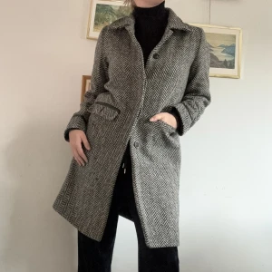 Svartvit ullkappa - Strl: S Mått: axelbredd 40cm, längd 90cm  Material: 40% ull, 35% akryl, 20% polyamid, 5% övriga fibrer  Modell: medellängd, rak passform Märke: KappAhl  Skick: använt skick (se sista bilden för en liten söm som stretchats ut) annars är den i fint skick! 