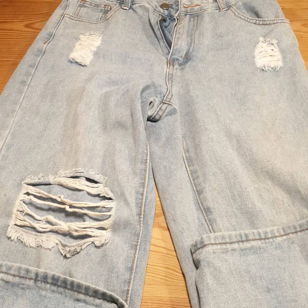 Ett par ljusblåa raka men lita utsvängda jeans med 3 hål, ett litet på båda låren och ett större på högerben. . Jeans & Byxor.