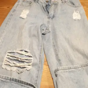 Ett par ljusblåa raka men lita utsvängda jeans med 3 hål, ett litet på båda låren och ett större på högerben. 