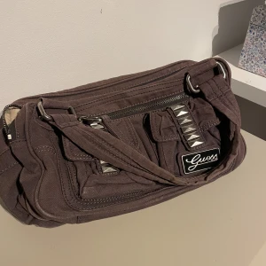 Vintage Guess Bag - Säljer en unik väska från guess, måtten är 30 cm i längd, 15 cm i höjd. Flera fickor och dragkedjor så det finns plats för mycket. Skriv för frågor/ fler bilder.