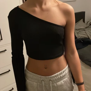 Tröja med bar axel - Svart topp med ena axeln bar och långärmad på andra sidan. Har inte använts många gånger alls så den är alltså i bra skick. Storlek 152