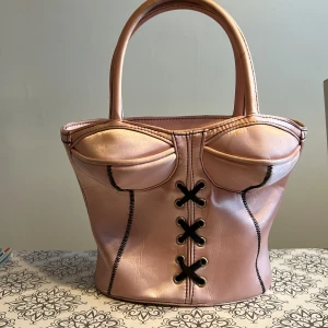 Handväska - Super fin handväska som föreställer en korsett💗 aldrig använd och i super fint skick. Vill du veta mått så kan du skriva. Super fin på insidan och har även en extra ficka på insidan. Så fin rosa färg💗