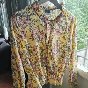 Gina tricot blus - Fin blus med detaljer som knytning i kragen och knappar. Använd en gång och är i fint skick. Finns djur i hemmet så kan förekomma katthår. Bredd : 40 cm, längd: 53 cm