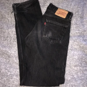 Levis 501 - Svart/grå vintage Levis 501 jeans. Bra skick för att vara från ca tidigt 90 tal. Finns en klippt kort slits i benen. Sitter baggy och är väldigt långa på mig som vanligtvis har storlek 36, är 168cm lång. 