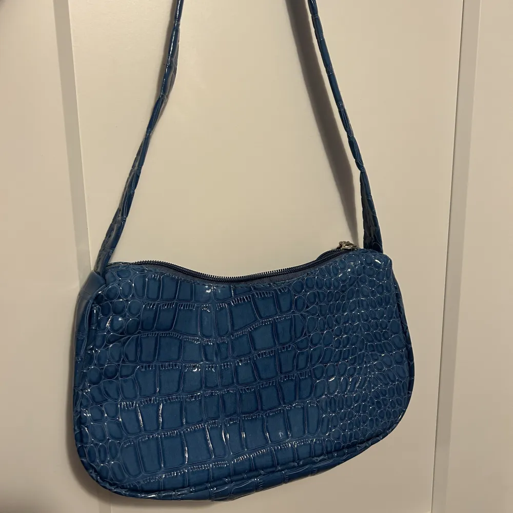 En axelväska i en jättefin blå färg och i ett krokodilmönster. Är i bra skick och nästan helt oanvänd, kommer inte till användning då jag köpt massa väskor . Väskor.