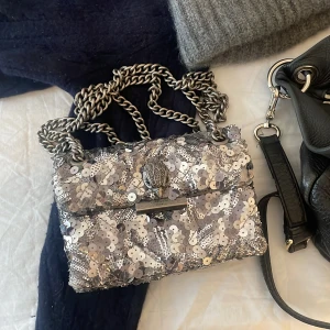 Kurt Geiger väska - Säljer nu min älskade silver glittriga Kurt Geiger väska💕💕 Väskan är i mini storleken och har vissa defekter på baksidan, där paljetterna lossnat (se andra bilden)! Dustbag tillkommer även!