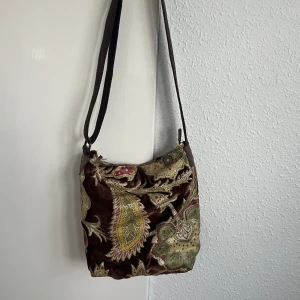 Väska - Väska från Ceannis. Lagom storlek med många användbara fack samt en nyckelhållare. Bandet kan justeras till önskvärd längd. Tecken på användning finns men fortfarande i mycket bra skick. :) Nypris ca 650kr Mått ca 20x26x9 cm