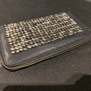 Plånbok från cowboysbag - Svart läderplånbok med nitar. Många fack. Stängs med dragkedja.  Från cowboysbag