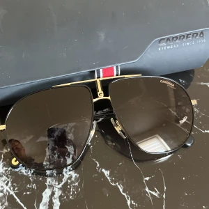 Carrera solglasögon  - Solglasögon av märket Carerra , äkta och inköpta på mister spex. Aldrig använda , bara testade. Inga repor eller skador. Färgen är åt mörkbrunt. Originalbox till glasögonen medföljer 