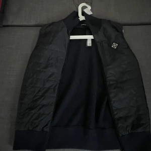 J.Lindberg Becket Hybrid Zip Vest - En mångsidig och modern design som kombinerar elegans med funktionalitet. Tillverkad med högkvalitativa material för att ge optimal värme och rörelsefrihet. Vid intresse eller frågor, kontakta gärna vid ytterligare information.