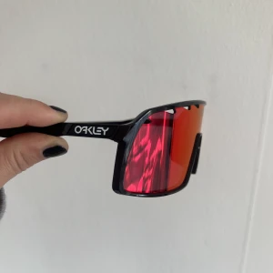 OAKLEY nya glasögon. Solglasögon / skidglasögon  - Nya glasögon från OAKLEY  Passar som solglasögon eller skidglasögon. Jättebra ljus så man vill inte ens ta av sig dom. Det kommer med ett fodral. Det står helsvarta på förpackningen men det är rosa/röd lins. Har fler i min annons, går att byta lins