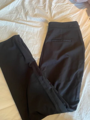 Svarta kostymbyxor med slits - Svarta raka kostymbyxor med slits från NA-KD i storlek 42 och hög midja. 150kr plus frakt 