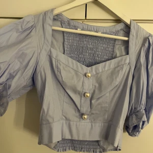 Pärltopp från Zara - Croppad blus från Zara med pärldetaljer fram, färgen blå. Armarna är puffiga. Storlek Xs men lite större i storleken, passar mer på större byst. Endast använd 1 gång. 