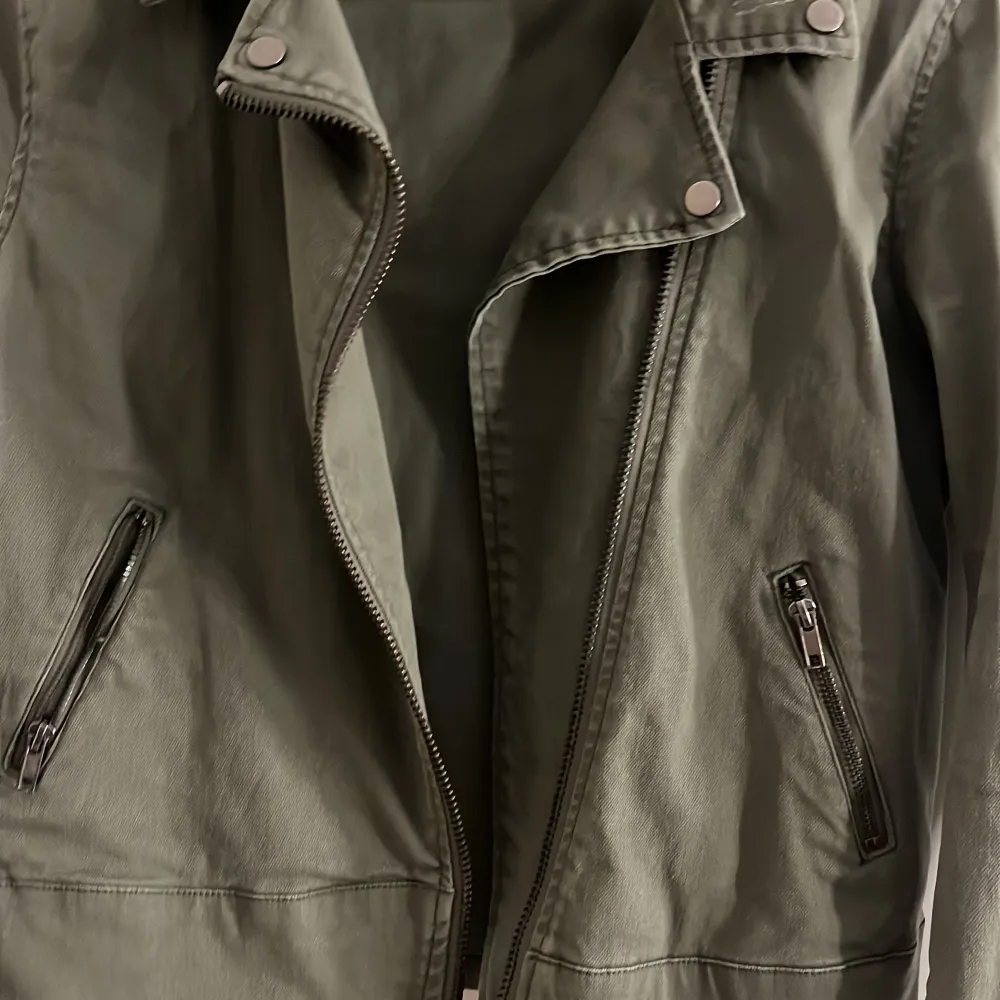 En oliv grön långärmad jeans jacka som har dragkedjor vid handleden och en sne dragkedja i mitten, sedan en normal dragkedje ficka på sidorna. Den är i bra skick och använt fåtals gånger. . Jackor.