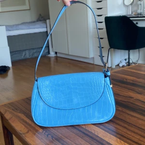 Blå Axelväska - Tryck gärna på ”köp nu” för billigare o spårbarfrakt 🥰 Gullig krokodilmönstrad ljusblå axelbandsväska. Bredd: 26cm Höjd: 16cm. Justerbart axelband (syns på bild 2) så går att göra bandet längte. Slängs med magnet-knapp. Knappt använd så i fint skick 💙