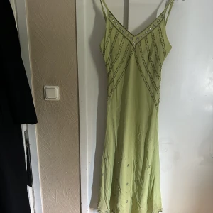 Grön midiklänning med detaljer  - En superfin ljusgrön midiklänning från indiska. Den har påsydda paljetter, figursydd och sitter jättefint på! Storlek L. Fint skick, inga defekter. 