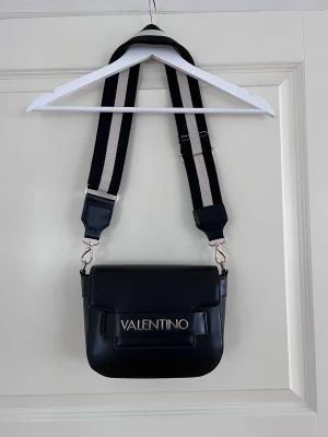 Väska från Valentino by mario valentino - En superfin och unik väska från Valentino by Mario Valentino. Väskan har ett justerbart band, ett stort fack som går att försluta med dragkedja samt två mindre sidofack. En liten fläck på axelbanden (se bild) men annars i väldigt fint skick!! 