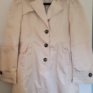 Snygg kappa! Helt ny!! - Den här jättesnygga kappan är aldrig använd, därav att den ser ostruken ut. Jag säljer den eftersom att jag redan har en liknande. Det är knappar framtill och i rygg, i en lätt figursydd modell. Rynkiga och trendiga axlar.