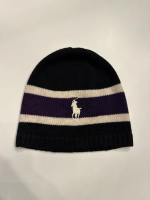 Ralph lauren mössa - Ralph lauren mössa i färgerna svart,vit och lila. Materialet är i stickad form. Säljer eftersom den ej passar längre. Som helt ny, endast testad fast etikett saknas (20diameter).