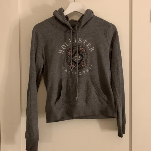 Hollisterhoodie - En grå hollisterhoddie lite sliten men fortfarande i väldigt bra skick väldigt skön och är lätt att matcha fits med. 
