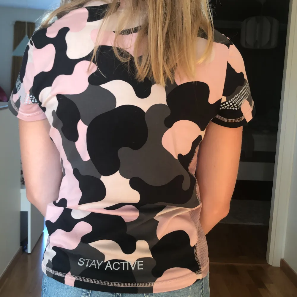 En tränings tröja som är kamoflerad med färgerna: Rosa, grå och svart! Har små reflexer på ärmarna och en liten text där det står: Stay Active. T-shirts.
